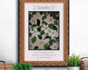 May include: A framed wall art piece featuring a central painting of white flowers and green leaves. The text 2 Timothy 1:7 is printed at the top, and the verse For the Spirit God gave us does not make us timid, but gives us power, love, and self-discipline is printed at the bottom. The frame is ornate and metallic gold.