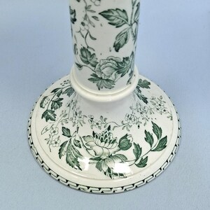 K&ouml;nnte beinhalten: Ein wei&szlig;er Kerzenst&auml;nder aus Keramik mit einem gr&uuml;nen Blumenmuster. Der Sockel ist rund mit einem detaillierten Rand, und der Stiel ist zylindrisch. Das Design zeigt Rosen und Bl&auml;tter und schafft einen klassischen, eleganten Look. Geeignet f&uuml;r die Inneneinrichtung.