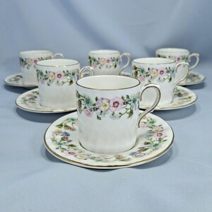 Peut inclure: Un ensemble de tasses et soucoupes en porcelaine blanche. Chaque tasse et soucoupe est orn&eacute;e d'un motif floral rose, jaune et bleu. Les bords des tasses et des soucoupes sont dor&eacute;s.