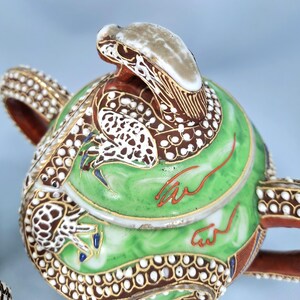 Pu&ograve; includere: Teiera ornata con un design a serpente. La teiera presenta un corpo verde con dettagli marroni e bianchi, finiture dorate e un beccuccio a forma di testa di serpente. Anche il manico e il bordo sono decorati con motivi intricati.