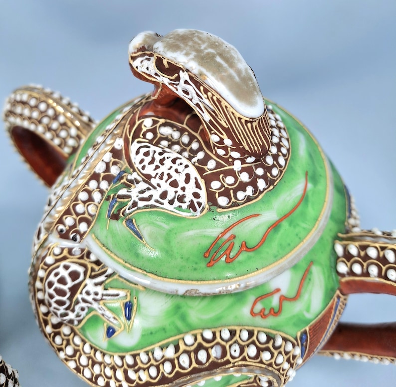 Pu&ograve; includere: Teiera ornata con un design a serpente. La teiera presenta un corpo verde con dettagli marroni e bianchi, finiture dorate e un beccuccio a forma di testa di serpente. Anche il manico e il bordo sono decorati con motivi intricati.