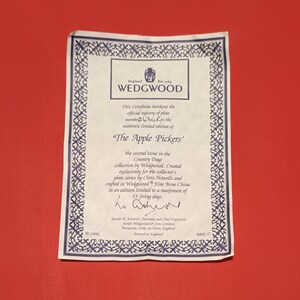 Pode incluir: Um certificado de autenticidade para um prato Wedgwood "The Apple Pickers". O certificado &eacute; branco com uma borda preta e apresenta o logotipo da Wedgwood. O texto no certificado indica que o prato faz parte da cole&ccedil;&atilde;o Country Days e &eacute; limitado a 55 dias de cozimento.