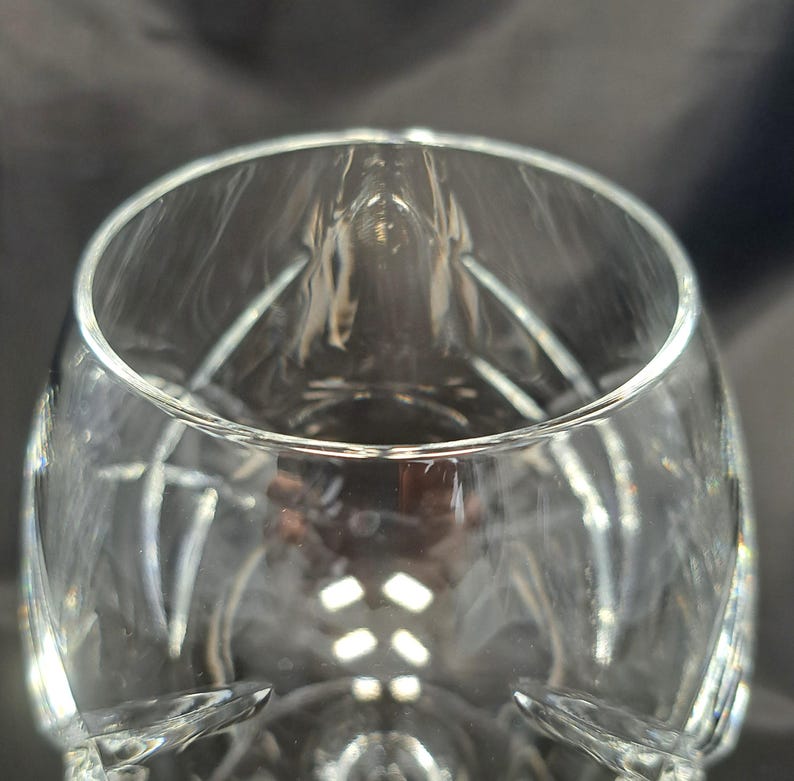 Puede incluir: Una copa de cristal transparente con un cuerpo ancho y redondeado y un borde estrecho. El cristal presenta una serie de facetas verticales talladas que crean un patr&oacute;n geom&eacute;trico texturizado en la superficie exterior, reflejando la luz.
