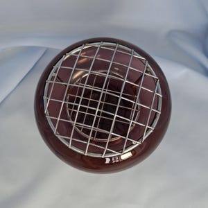 Puede incluir: Un jarr&oacute;n redondo de cristal morado oscuro con un inserto de rejilla met&aacute;lica plateada. El jarr&oacute;n tiene un acabado brillante y una forma esf&eacute;rica. El inserto de rejilla est&aacute; hecho de finos alambres met&aacute;licos que se cruzan, creando un patr&oacute;n geom&eacute;trico. El jarr&oacute;n se utiliza probablemente para arreglos florales.