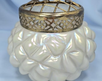 May include: A white, iridescent glass flower frog with a textured, quilted pattern. It has a decorative, gold-toned metal grid and filigree rim. The flower arranging tool is designed to hold flowers in place.