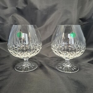 May include: A pair of clear crystal brandy snifters featuring a deep diamond-cut pattern on the lower bowl and a starburst design on the circular base. Each glass has a small circular green sticker applied to the upper side of the bowl.
