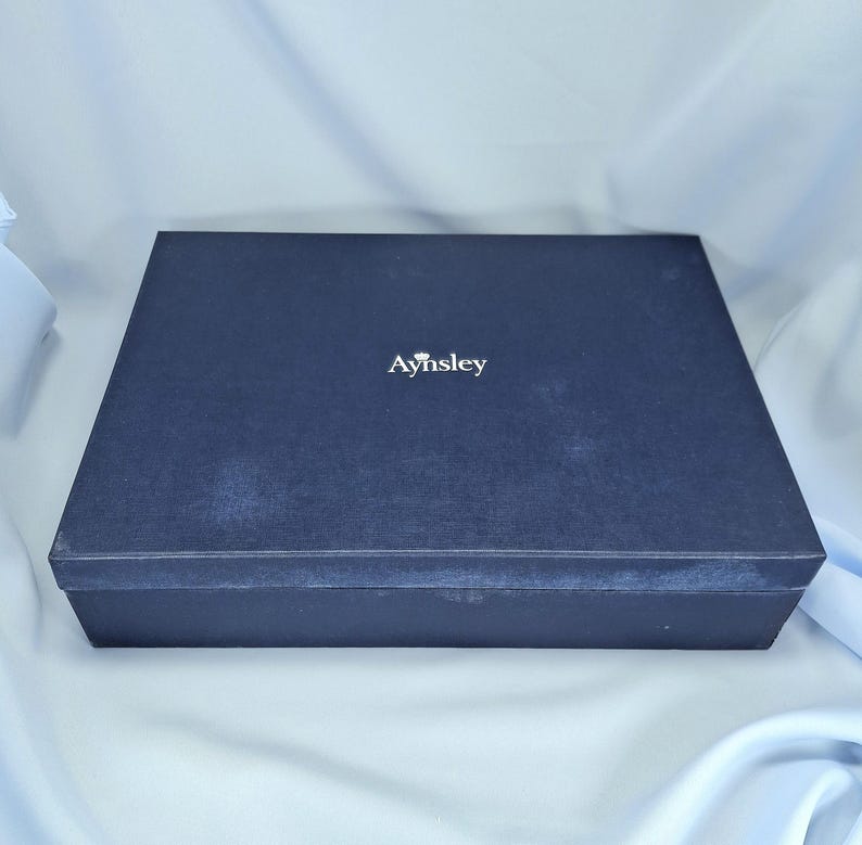 Peut inclure: Une bo&icirc;te rectangulaire bleu marine fonc&eacute; avec le mot "Aynsley" en lettres blanches. La bo&icirc;te a une surface textur&eacute;e et un design simple et &eacute;l&eacute;gant, adapt&eacute; au stockage ou au cadeau.
