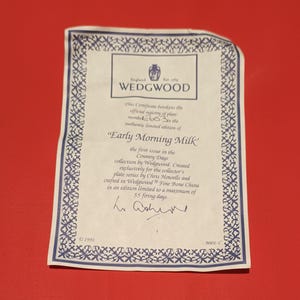 Pode incluir: Um certificado branco com borda e texto azuis. O certificado &eacute; para um prato Wedgwood "Early Morning Milk", a primeira edi&ccedil;&atilde;o da cole&ccedil;&atilde;o Country Days. O certificado &eacute; numerado 603 e assinado por "W. Ashworth".