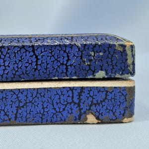 May include: Close-up of two blue boxes with a textured, cracked pattern. The boxes are stacked on top of each other, with the top box slightly overlapping the bottom one. The edges of the boxes show signs of wear.