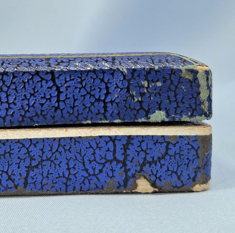 May include: Close-up of two blue boxes with a textured, cracked pattern. The boxes are stacked on top of each other, with the top box slightly overlapping the bottom one. The edges of the boxes show signs of wear.