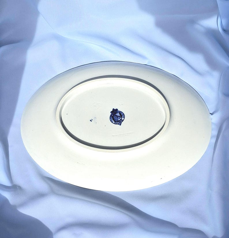 May include: The underside of a white oval serving platter with a blue and white crest in the center. The crest features a crown and a lion.