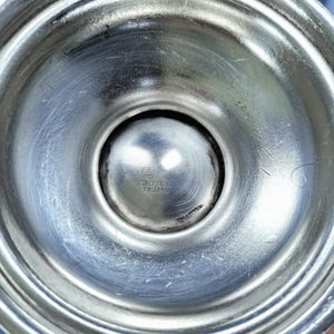 K&ouml;nnte beinhalten: Nahaufnahme eines silberfarbenen Metallobjekts, m&ouml;glicherweise ein Kerzenst&auml;nderfu&szlig;. Der Fu&szlig; hat eine abgerundete, konkave Form mit konzentrischen Ringen und einem zentralen, kugelf&ouml;rmigen Detail. Der Text "SHEFFIELD ENGLAND" ist sichtbar.