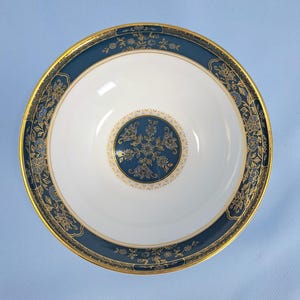 Op de afbeelding: Een ronde keramische kom met een wit midden en een cirkelvormig blauw en goudkleurig bloemenmedaillon. De brede rand is diepblauw met een goudkleurig bloemmotief en een dunne goudkleurige rand. Het binnenoppervlak is glad en glanzend.