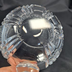 Op de afbeelding: Een heldere, zware glazen kom met ingewikkelde geslepen patronen, waaronder stermotieven en verticale ribbels langs de buitenrand. De kom heeft een dikke, transparante basis en een gepolijst, reflecterend oppervlak met scherpe, geometrische randen.
