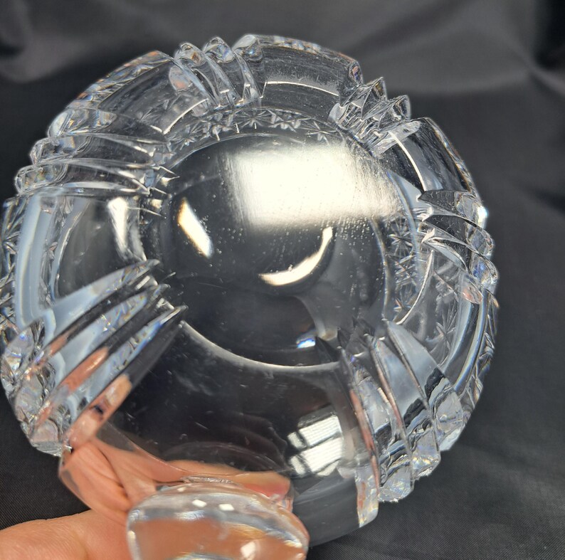 Op de afbeelding: Een heldere, zware glazen kom met ingewikkelde geslepen patronen, waaronder stermotieven en verticale ribbels langs de buitenrand. De kom heeft een dikke, transparante basis en een gepolijst, reflecterend oppervlak met scherpe, geometrische randen.