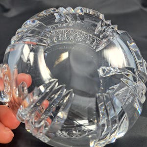 Op de afbeelding: Een heldere, zware kristallen kom met ingewikkelde, diep geslepen geometrische patronen en sterrenmotieven langs de dikke, geschulpte rand. Het glas is transparant met reflecterende facetten die het licht vangen, wat zorgt voor een schitterende, veelzijdige uitstraling over de gehele ronde structuur.