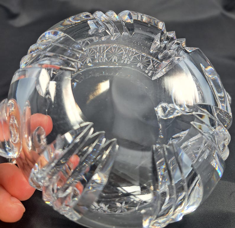Op de afbeelding: Een heldere, zware kristallen kom met ingewikkelde, diep geslepen geometrische patronen en sterrenmotieven langs de dikke, geschulpte rand. Het glas is transparant met reflecterende facetten die het licht vangen, wat zorgt voor een schitterende, veelzijdige uitstraling over de gehele ronde structuur.