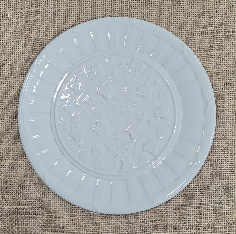 K&ouml;nnte beinhalten: Hellblaue Keramikplatte mit detailliertem Blumen- und Bl&auml;ttermuster in der Mitte. Der Teller hat einen gerippten Rand und eine glatte, gl&auml;nzende Oberfl&auml;che. Der runde Teller hat einen Durchmesser von etwa 25 cm.