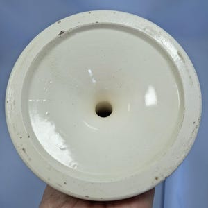 K&ouml;nnte beinhalten: Nahaufnahme des Bodens einer cremefarbenen Keramikvase. Die Vase hat einen breiten, kreisf&ouml;rmigen Boden mit einem zentralen Loch. Der Rand des Bodens ist leicht strukturiert und weist Gebrauchsspuren auf. Die Innenfl&auml;che ist glatt und gl&auml;nzend.