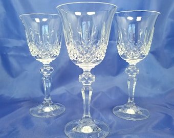 May include: Three clear crystal wine glasses featuring a diamond-cut pattern on the lower bowl and a faceted, hexagonal-shaped stem. Each glass has a wide, flared rim and a circular base, reflecting light through the intricate glass carvings.