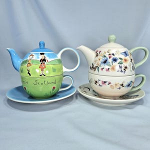 Puede incluir: Dos tazas de té y teteras decorativas. Un juego presenta un diseño de cielo azul y campo verde con figuras escocesas y el texto "Annie Scotland". El otro juego tiene un diseño floral y de mariposas con un asa verde.