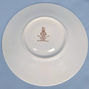 May include: A white fine bone china saucer with a central brown stamp reading Royal Doulton England, English Fine Bone China, Carlyle, H. 5018, Copyright Doulton & Co. Limited, featuring a crown and lion emblem in the centre of the circular base.