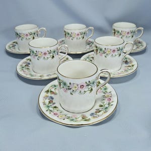 Peut inclure: Service &agrave; th&eacute; de six pi&egrave;ces avec tasses et soucoupes blanches. Les tasses et les soucoupes sont d&eacute;cor&eacute;es d'un motif floral avec des fleurs roses, jaunes et bleues. Les bords sont dor&eacute;s. Les tasses ont une surface textur&eacute;e.