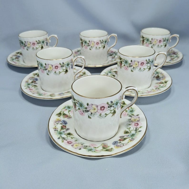Peut inclure: Service &agrave; th&eacute; de six pi&egrave;ces avec tasses et soucoupes blanches. Les tasses et les soucoupes sont d&eacute;cor&eacute;es d'un motif floral avec des fleurs roses, jaunes et bleues. Les bords sont dor&eacute;s. Les tasses ont une surface textur&eacute;e.