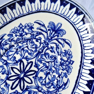 May include: A white ceramic plate with a blue and white floral design. The plate has a scalloped edge and a blue rim.