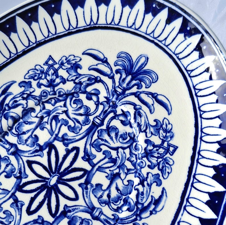 May include: A white ceramic plate with a blue and white floral design. The plate has a scalloped edge and a blue rim.
