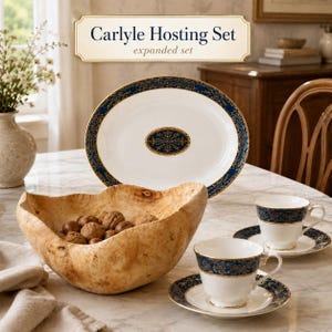 May include: The Carlyle Hosting Set expanded set includes a white oval platter with a dark blue and gold filigree border and central medallion, two white teacups with matching blue and gold rims on saucers, and a large, natural light brown wooden bowl.