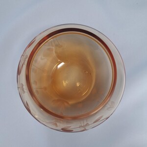 May include: A top-down view of a round, amber-colored glass bowl featuring a delicate, etched floral pattern around its exterior rim. The glass has a smooth, translucent finish, and the circular opening reveals the deep, warm orange interior.