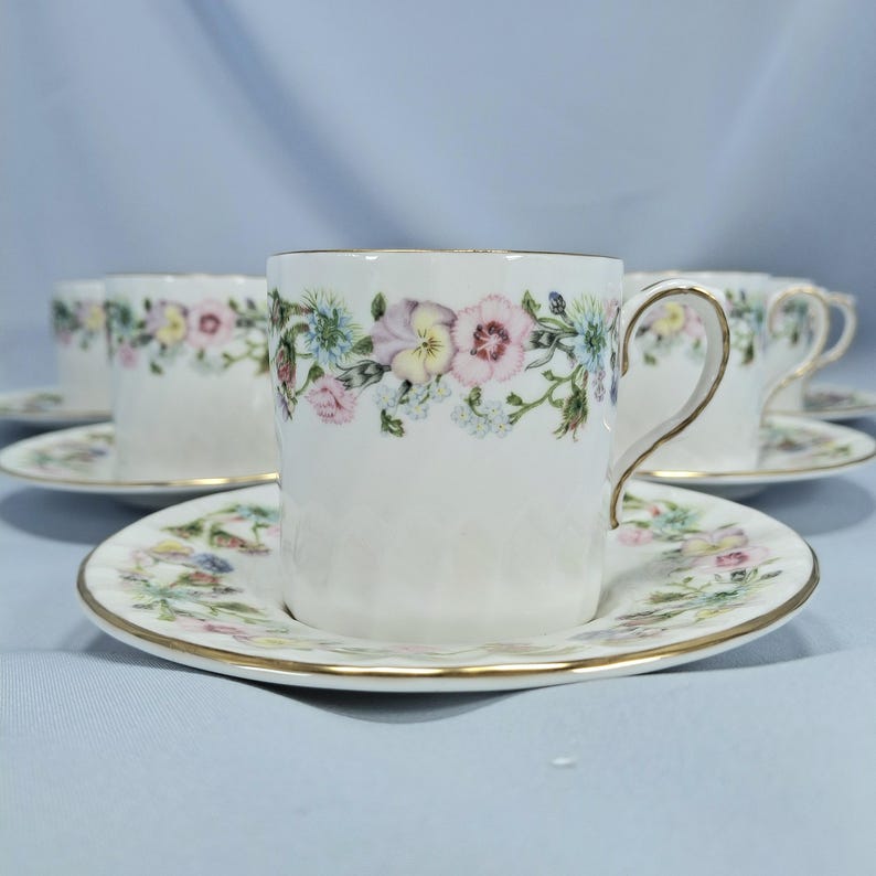 Peut inclure: Ensemble de tasses et soucoupes blanches avec un motif floral. Les tasses ont des bordures et des anses dor&eacute;es. Les soucoupes et les tasses sont d&eacute;cor&eacute;es d'un motif floral color&eacute; de fleurs roses, jaunes et bleues.