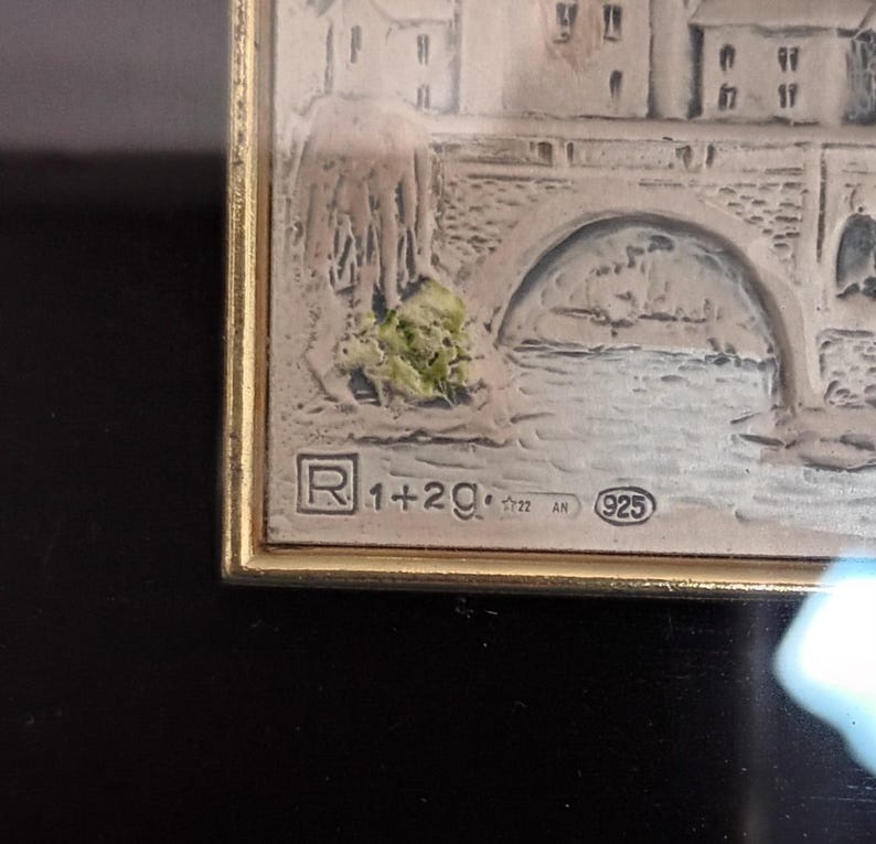 Puede incluir: Una obra de arte enmarcada en plata que representa un puente sobre un r&iacute;o con edificios en el fondo. El marco tiene una placa de plata con el texto "R 1+2g. 925" y el a&ntilde;o "1722 AN".