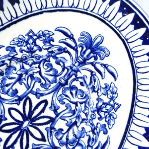 May include: A white ceramic plate with a blue and white floral design. The design features intricate swirls and leaves, with a central flower.