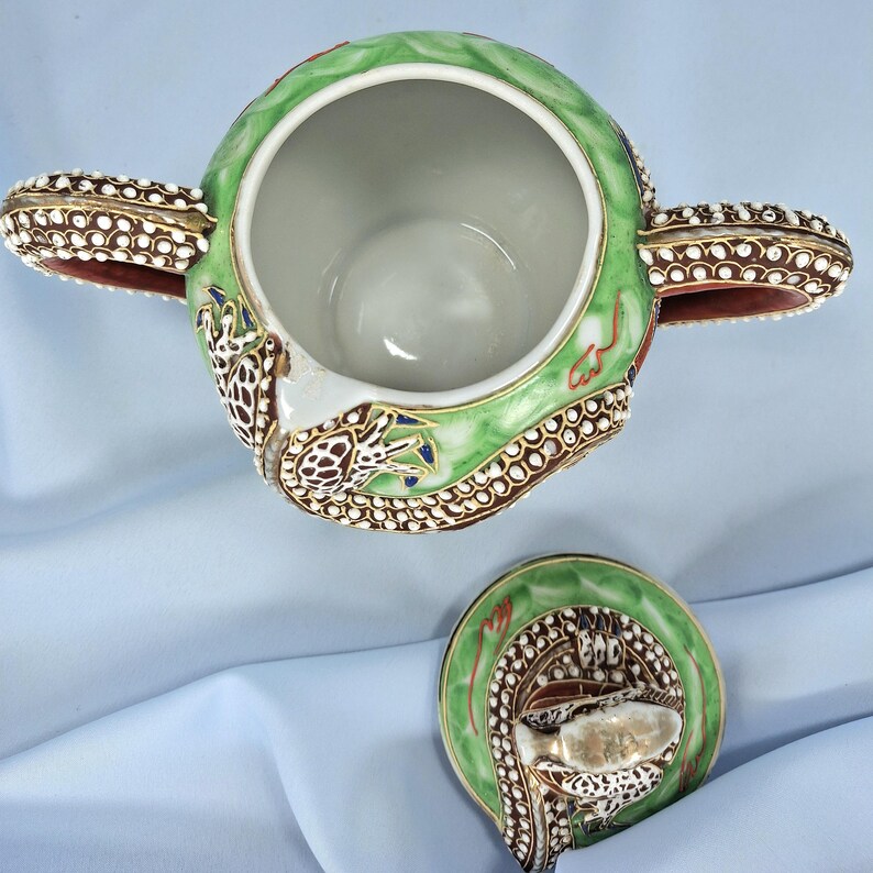Pu&ograve; includere: Vista dall'alto di una zuccheriera decorativa in ceramica con coperchio abbinato. La ciotola &egrave; principalmente verde con dettagli marroni e bianchi e presenta un motivo a drago. Il coperchio &egrave; a lato, mostrando l'interno della ciotola.