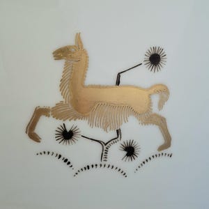 May include: A gold-colored llama illustration with black accents and starburst-like shapes. The llama is depicted in a running pose, with detailed fur and a stylized design. The background is plain white.