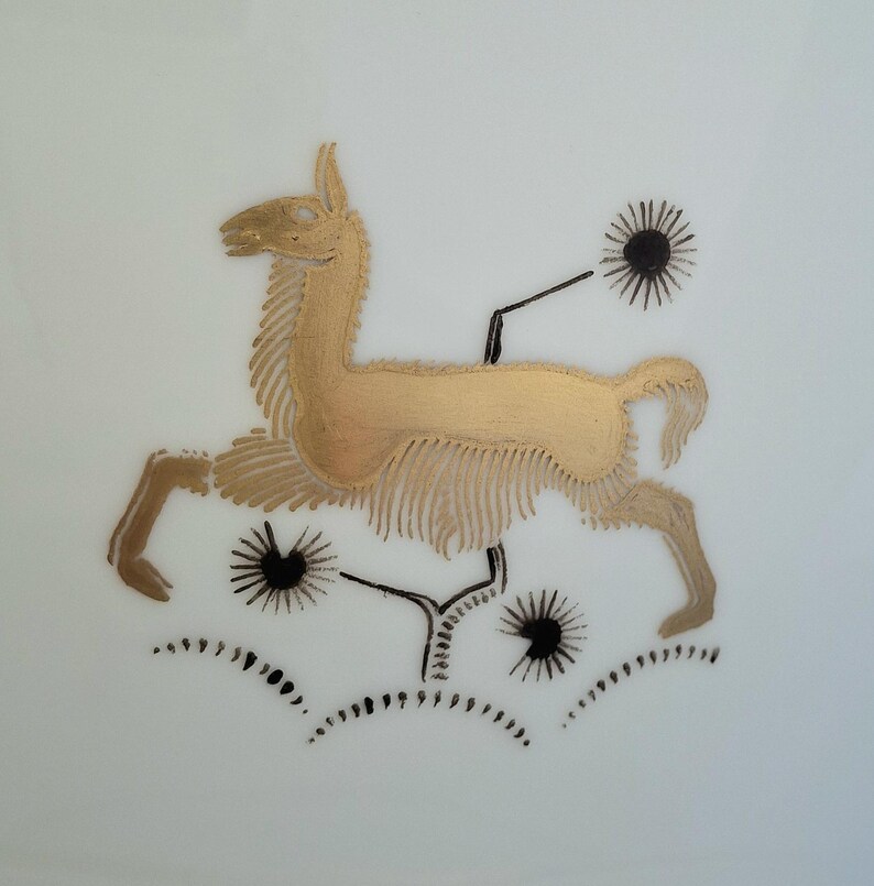 May include: A gold-colored llama illustration with black accents and starburst-like shapes. The llama is depicted in a running pose, with detailed fur and a stylized design. The background is plain white.
