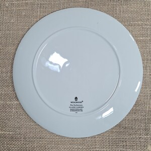 K&ouml;nnte beinhalten: Hellblaue Wedgwood Classic Garden Feinkeramik-Platte. Die Platte hat einen breiten Rand und eine leicht erh&ouml;hte Mitte. Das Wedgwood-Logo und Produktinformationen sind auf der R&uuml;ckseite aufgedruckt. Hergestellt in England.