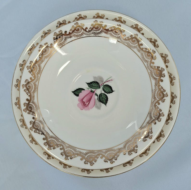 May include: A set of three white porcelain plates. The plates have a gold filigree border and a pink rose with green leaves in the centre. The plates are stacked on top of each other.