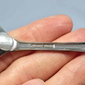 May include: Close-up of a silver spoon with a rounded bowl. The spoon's handle has the text "Sheffield England" engraved on it. The spoon is held in a person's hand.