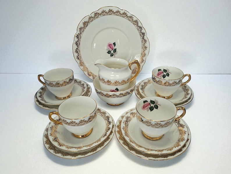 May include: A cream-coloured vintage tea set with gold detailing. The set includes teacups, saucers, a creamer, a sugar bowl, and a large serving plate. Each piece is decorated with a pink rose design, ideal for afternoon tea.