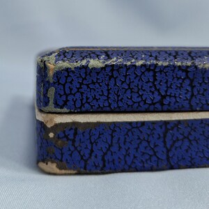 May include: Close-up of a blue box with a textured, cracked pattern. The box has a light-colored edge and shows signs of wear. The color is a deep, saturated blue, with a contrasting lighter edge.