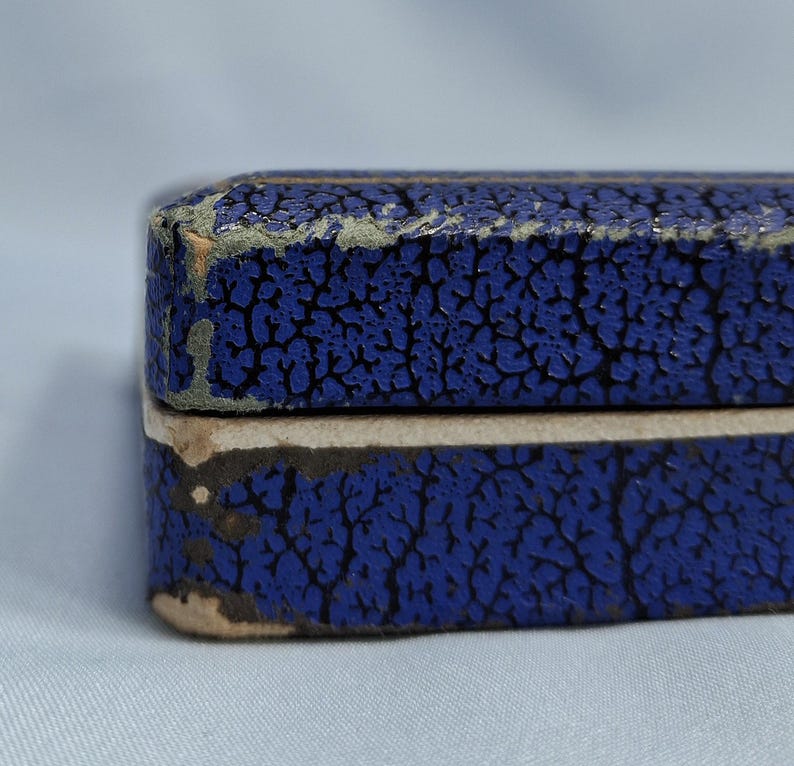 May include: Close-up of a blue box with a textured, cracked pattern. The box has a light-colored edge and shows signs of wear. The color is a deep, saturated blue, with a contrasting lighter edge.
