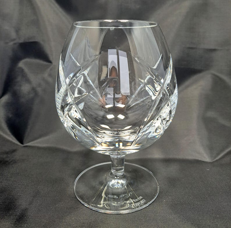 Puede incluir: Una copa de brandy de cristal transparente con un cuenco ancho y redondeado que presenta un patr&oacute;n de corte profundo en forma de diamante y cu&ntilde;a. La copa tiene un tallo corto y robusto y una base circular, con el texto John Rocha Waterford grabado.
