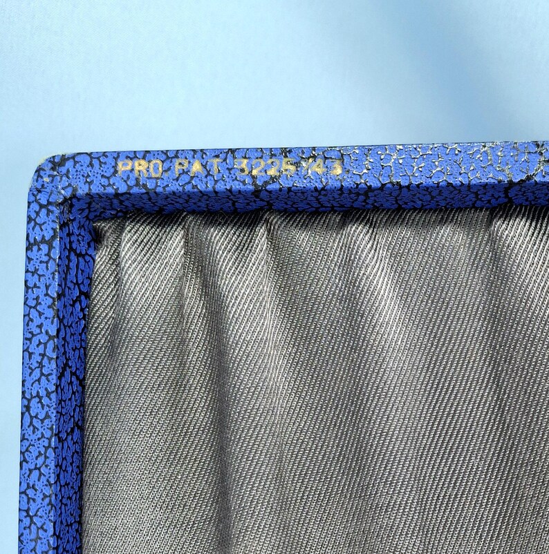 May include: Close-up of a blue box with a textured, patterned border and the text "PRO PAT 3225143" in gold lettering. The interior of the box is lined with gray fabric.