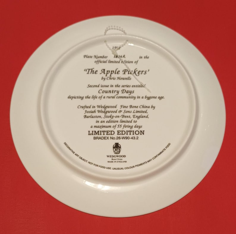 Pode incluir: Um prato de cer&acirc;mica branca com uma borda dourada e uma inscri&ccedil;&atilde;o em preto e dourado. A inscri&ccedil;&atilde;o diz "The Apple Pickers' by Chris Howells" e "Country Days depicting the life of a rural community in a bygone age." O prato faz parte de uma s&eacute;rie de edi&ccedil;&atilde;o limitada, elaborada em porcelana fina Wedgwood por Josiah Wedgwood & Sons Limited, Barlaston, Stoke-on-Trent, Inglaterra. O prato &eacute; uma edi&ccedil;&atilde;o limitada de 55 dias de cozedura e tem um n&uacute;mero Bradex de 26-W90-43.2.