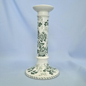 K&ouml;nnte beinhalten: Ein wei&szlig;er Kerzenhalter aus Keramik mit einem gr&uuml;nen Blumenmuster. Der Kerzenhalter hat einen breiten Sockel, einen hohen, zylindrischen K&ouml;rper und eine kleine, runde Oberseite zum Halten einer Kerze. Das florale Design bedeckt die gesamte Oberfl&auml;che.