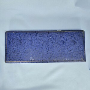 May include: A rectangular box with a textured, dark blue surface and a gold trim. The box has a pattern of black, vein-like lines across the top. The box is closed and appears to be empty.