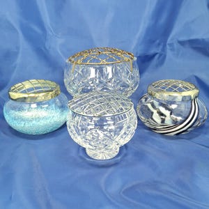 May include: Four glass flower frogs with metal grid inserts. One is light blue with white speckles, one is clear with a diamond pattern, one is clear with black and white swirls, and one is a large clear bowl with a gold-toned wire grid.